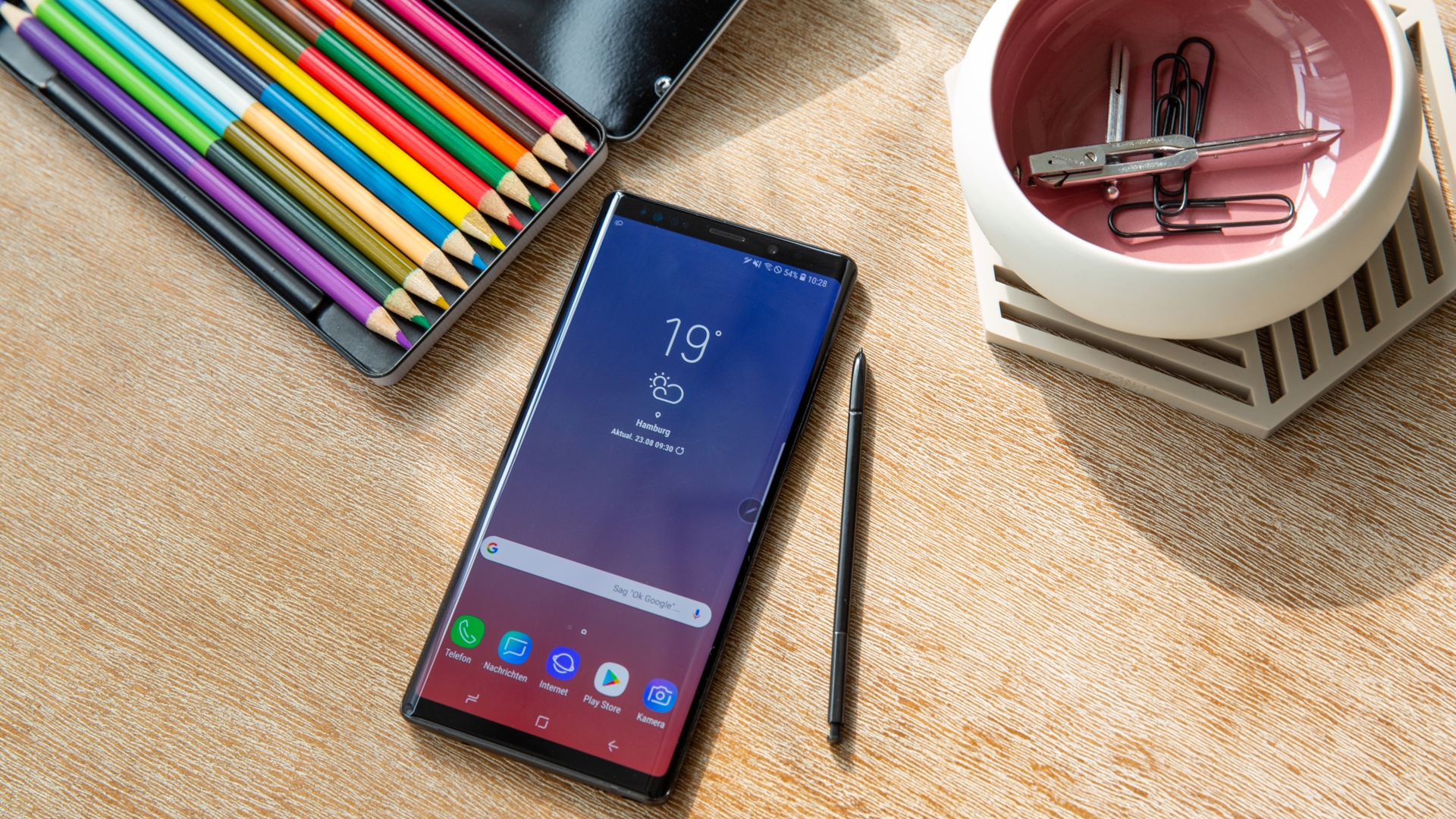 Galaxy Note 9 auf einem Schreibtisch neben einem Kasten voller Buntstifte.