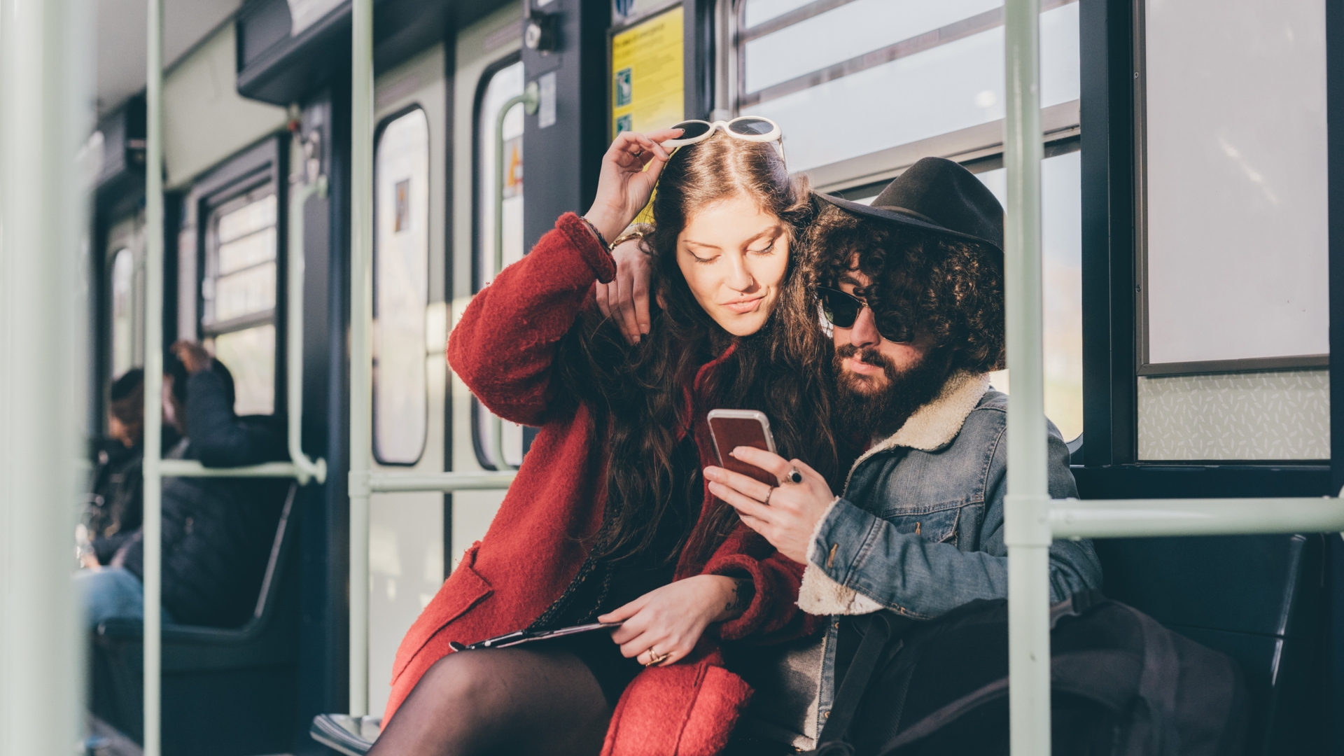 Young couple sitting on subway train, looking at smartphone