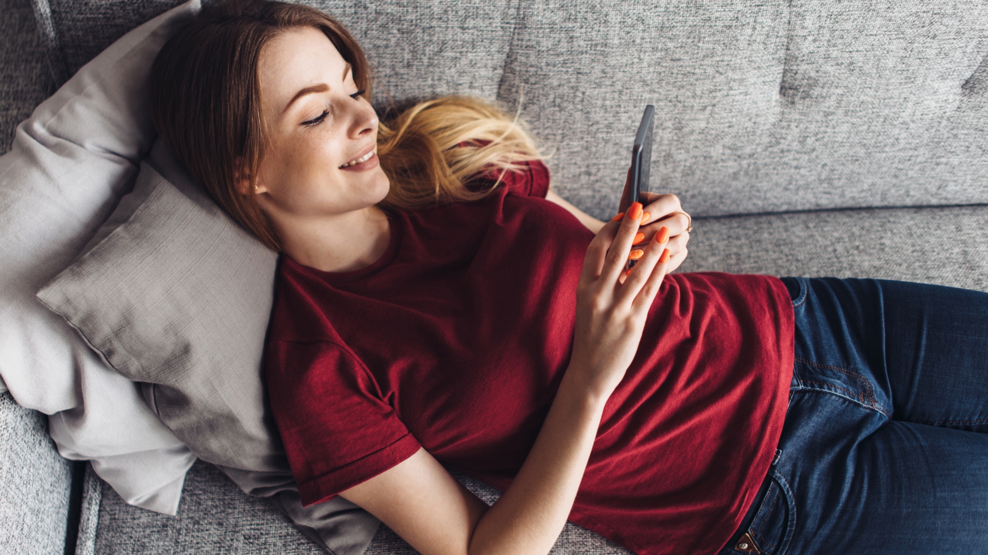 Frau tippt lächelnd auf der Couch auf ihr Handy