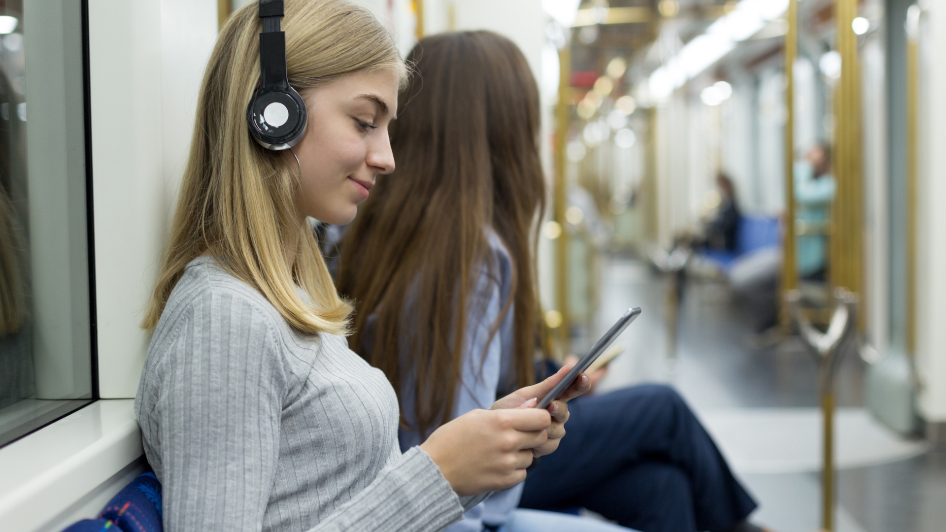 Junge Frau mit Kopfhörer und Tablet in der U-Bahn