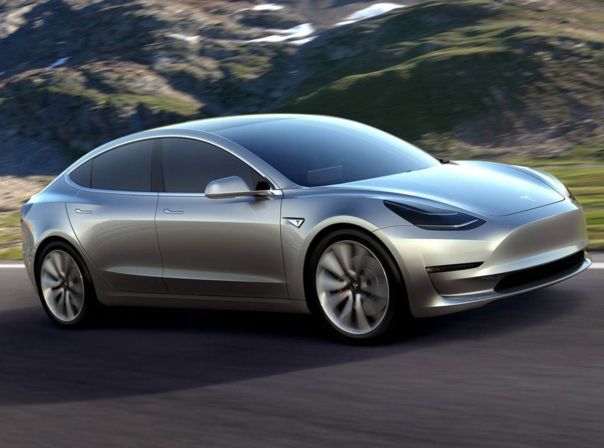 Silberner Tesla Model 3 fährt durch Gebirgsstraßen.