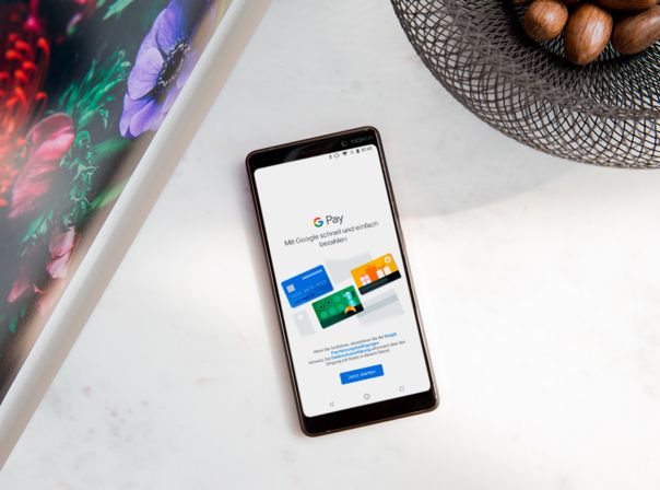 Smartphone mit geöffneter "Google Pay"-App auf einem weißen Tisch.