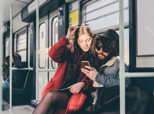 Young couple sitting on subway train, looking at smartphone