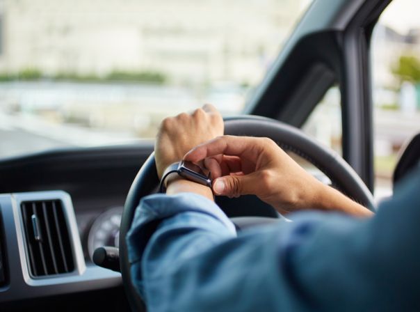 Autofahrer betätigt Smartwatch am Steuer.