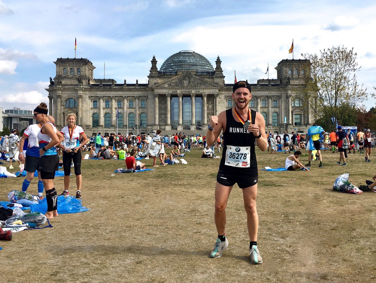 Lars Sonnemann jubelt mit der Medaille des Berlin Marathon vor dem Bundestag.