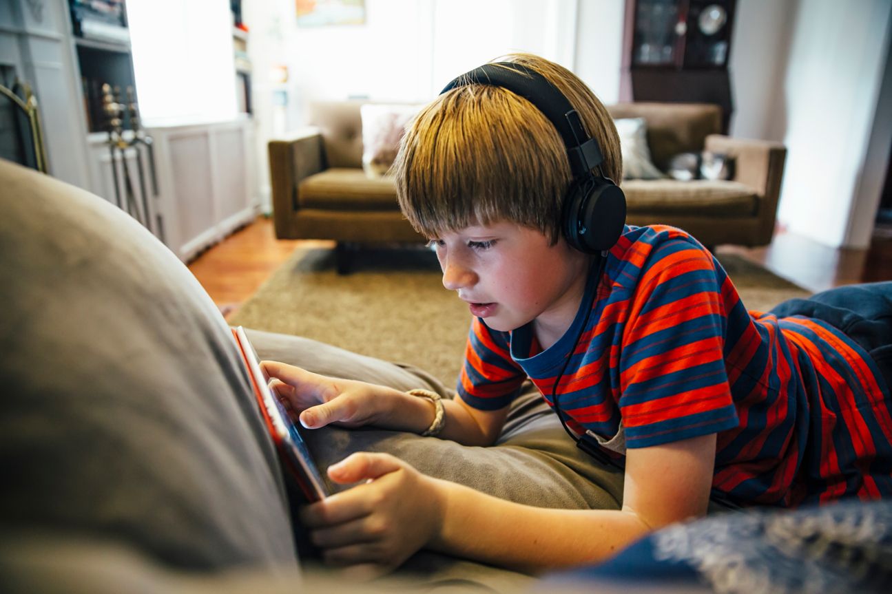 Junge mit Kopfhörern und Tablet auf Sofa